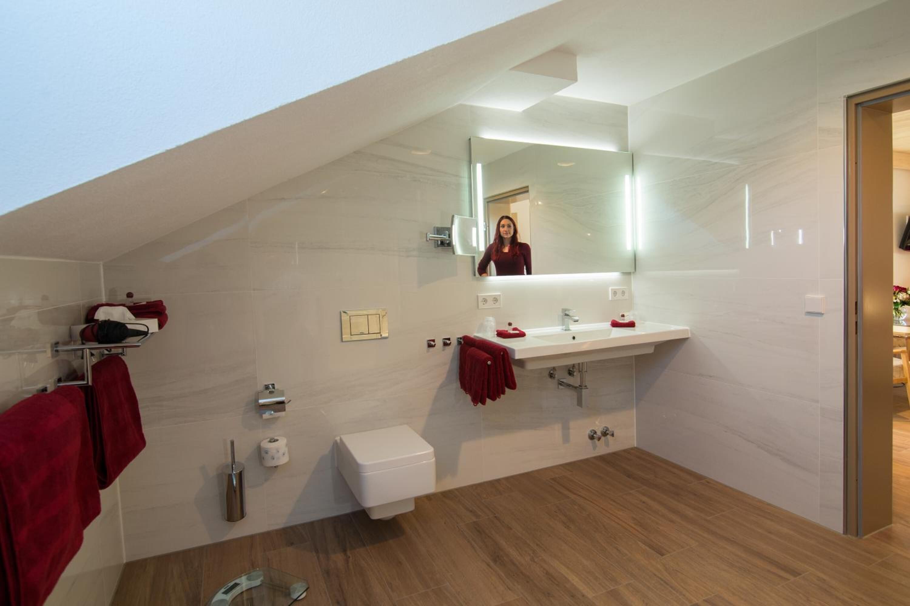 A modern bathroom with a large mirror, two sinks, a toilet, and a shower area.