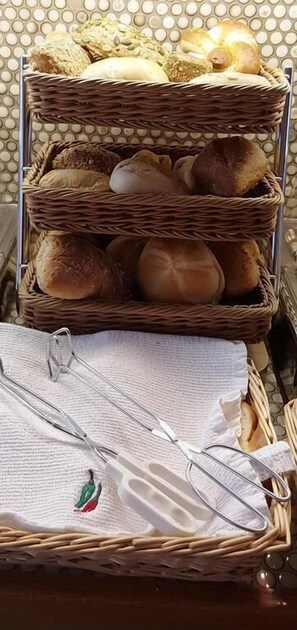 A three-tiered wicker basket filled with various breads and rolls, placed on a metal rack. - Hotel Garni Jägerhof (Sigmaringen)