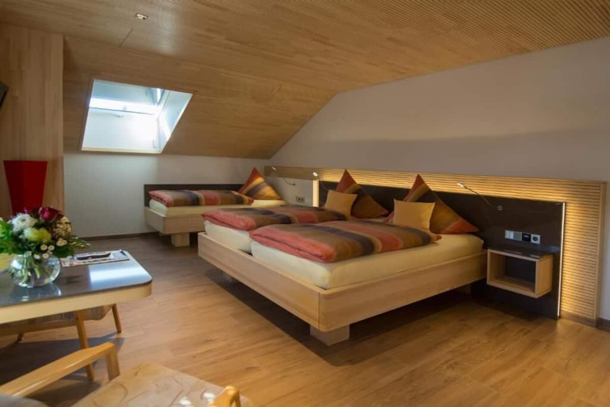 A modern bedroom with a sloped ceiling, a large bed with multiple pillows, a bedside table, and a small bedside lamp.