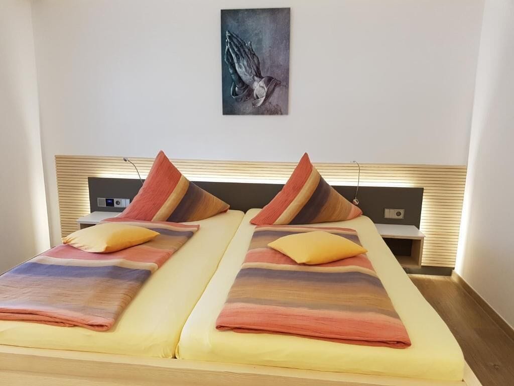 Uma cama de casal com manta degradê, duas almofadas e uma obra de arte na parede.