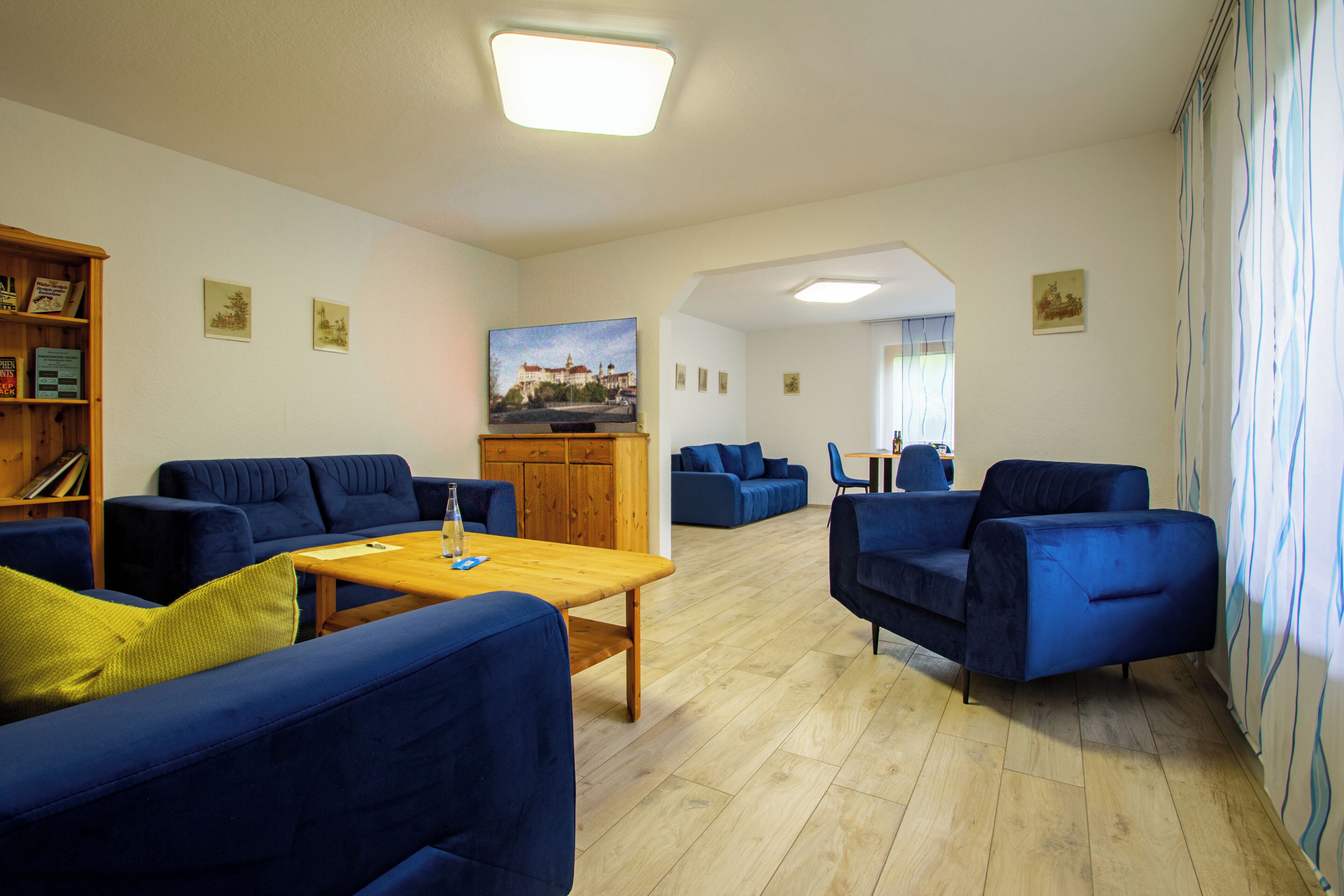 A spacious living area with blue sofas, a wooden coffee table, and a television on a wooden cabinet.