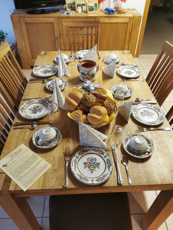 A wooden dining table set with floral-patterned plates, silverware, and a basket of bread. - Hotel Garni Jägerhof (Sigmaringen)