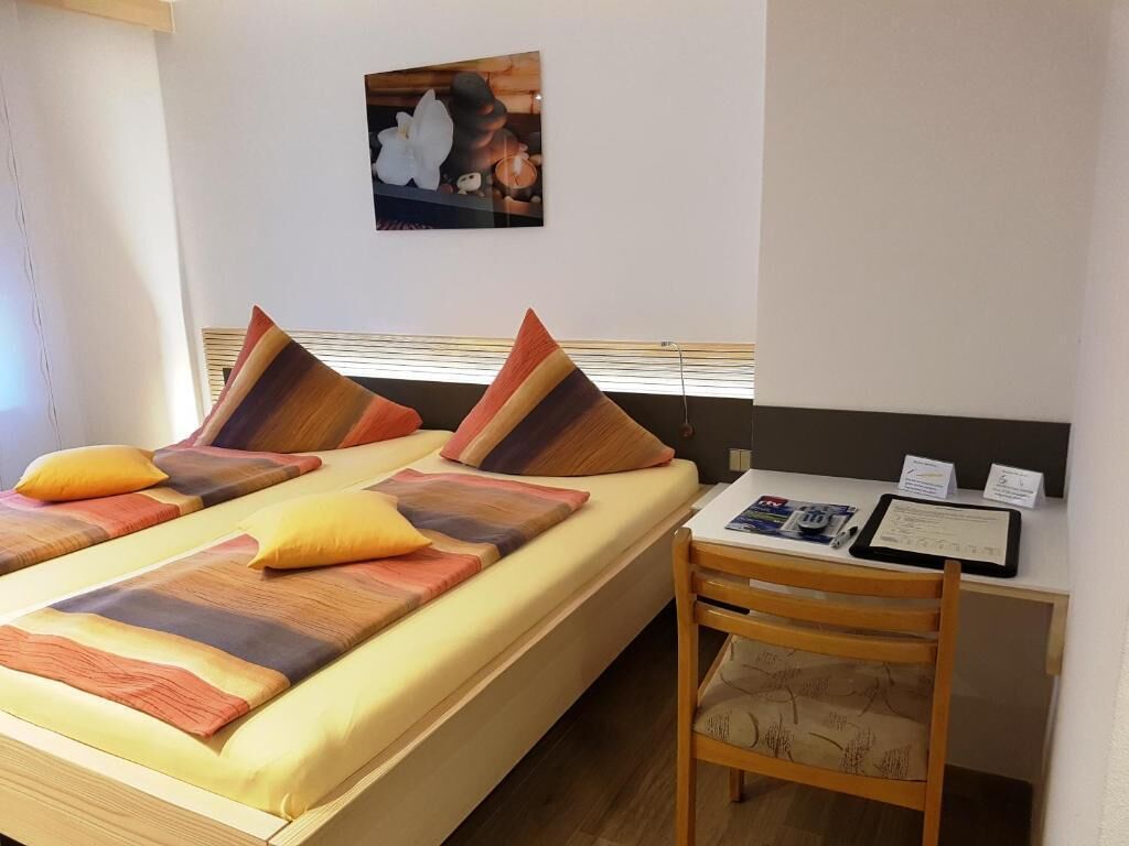 Habitación de hotel con cama, almohadas, escritorio y una silla, y un cuadro colgado en la pared.