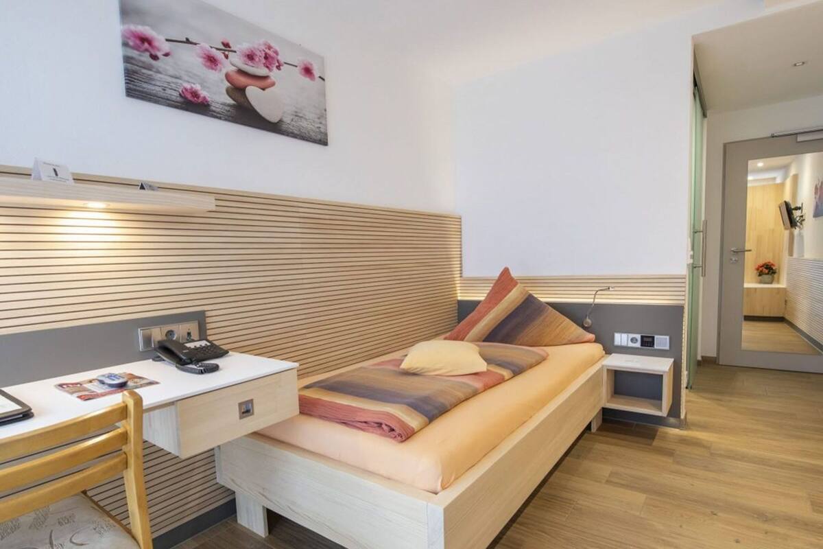 A modern hotel room with a bed, bedside table, and a desk with a telephone.