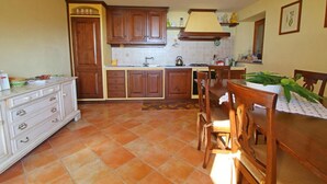 A kitchen with wooden cabinets, a tiled floor, a dining table with chairs, and a hanging light fixture. - Elcriso, Spacious villa, private pool, amazing views, WIFI, walk to restaurant! (Chiozza)