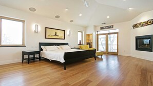 A spacious bedroom with a large bed, a nightstand, a chair, and a fireplace.