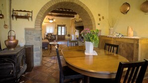 A dining area with a round wooden table, chairs, and a stone fireplace. - Spacious Tuscan Villa with Large Pool near Castiglion Fiorentino. (Castiglion Fiorentino)
