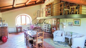 A spacious living area with a dining table, chairs, a staircase, and a bookshelf. - Spacious Tuscan Villa with Large Pool near Castiglion Fiorentino. (Castiglion Fiorentino)