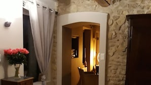 A stone-walled hallway with a wooden cabinet, a vase with flowers, and a door leading to another room. - Mas La Pomarède (Robion)