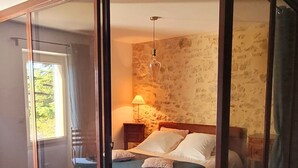 A bedroom with a bed, a nightstand, a lamp, and a view through a glass partition to a balcony. - Mas La Pomarède (Robion)