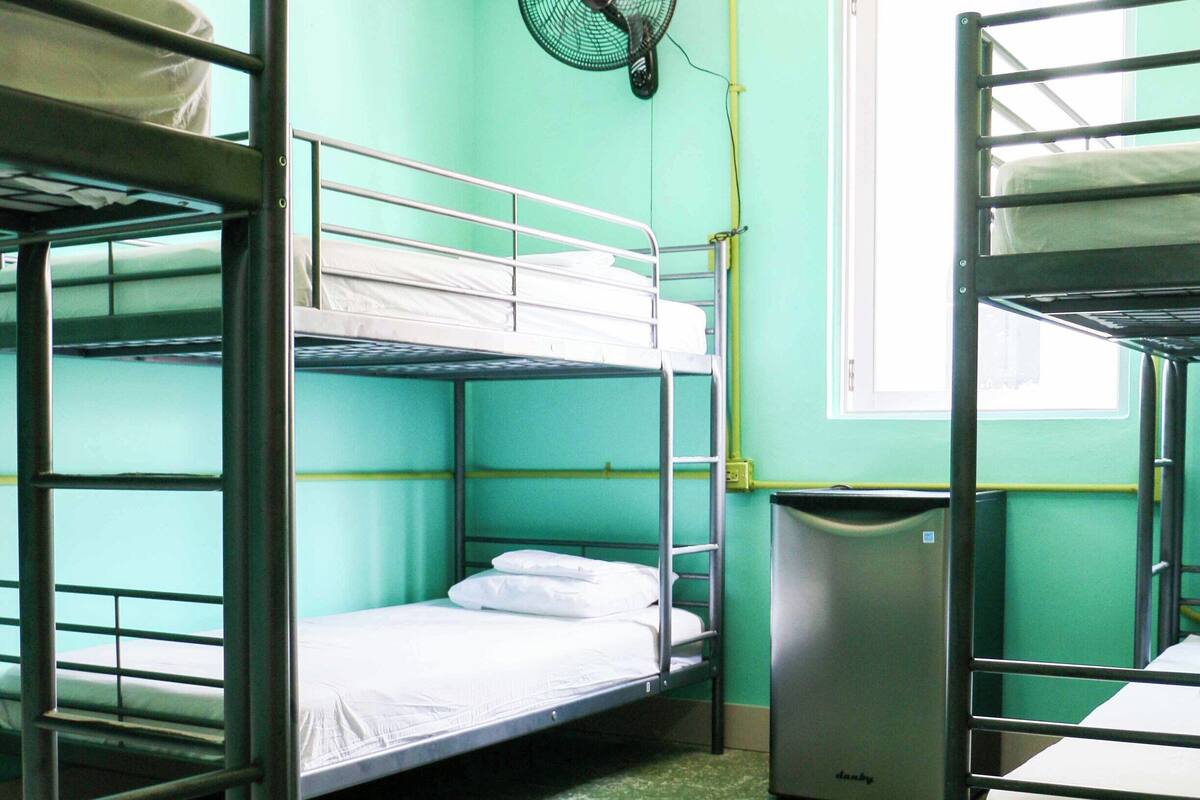 Un dormitorio con literas, un ventilador y un cubo de basura.