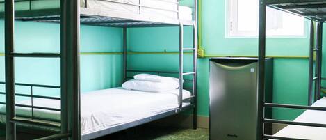 A dormitory room with bunk beds, a fan, and a trash bin.
