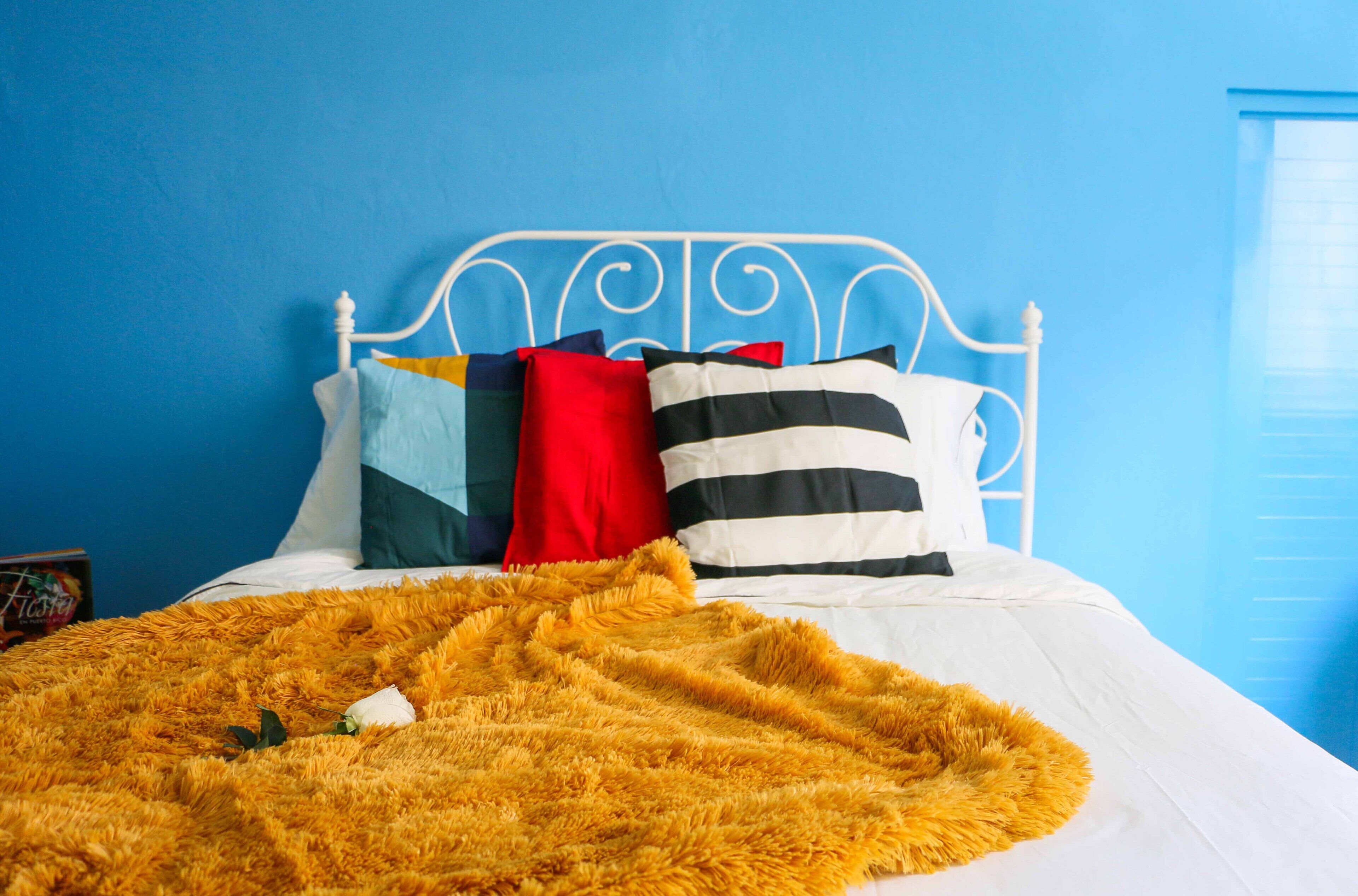 A bed with a white metal headboard, a yellow fluffy blanket, and multiple pillows in various colors.