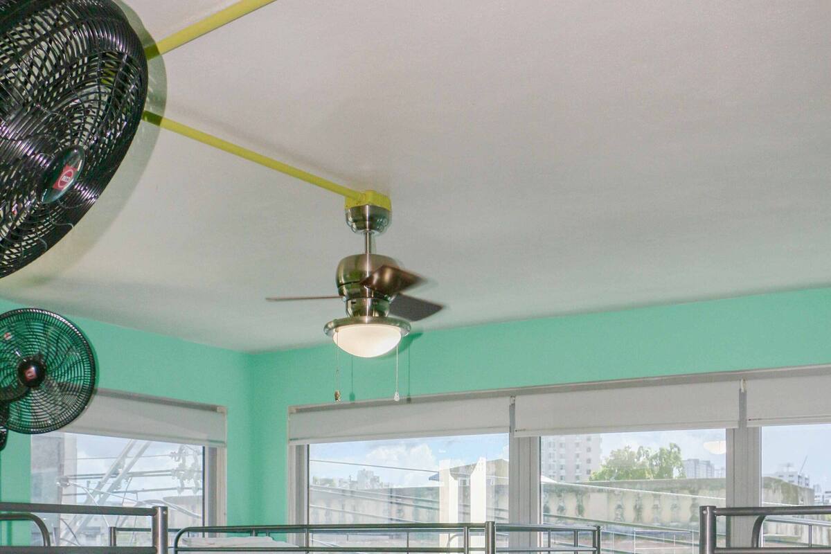Un dormitorio con literas, un ventilador de techo y ventanas amplias.