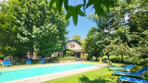Ein Pool mit Liegestühlen, umgeben von üppiger Vegetation und einem Steinhaus.