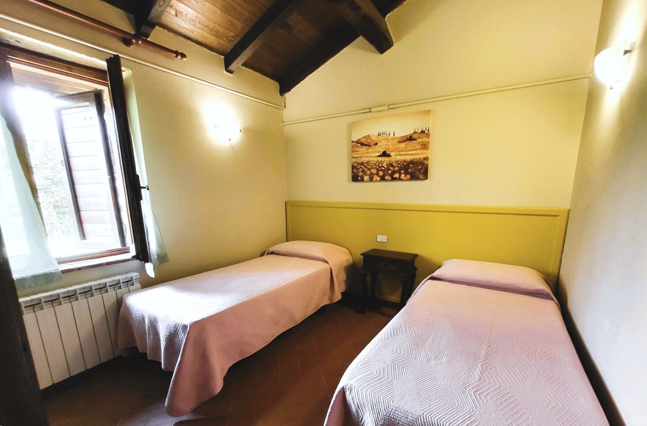 Ein Zimmer mit zwei Einzelbetten, einem Heizkörper, einem Fenster und einem Bild an der Wand.