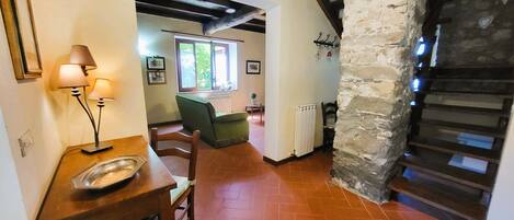 A rustic interior with a dining table, chairs, a sofa, and a stone pillar.