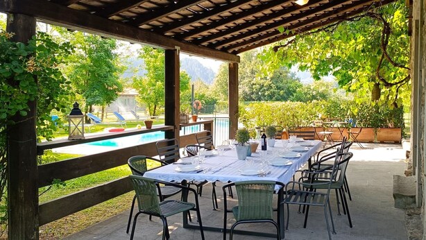 Eine Terrasse im Freien mit Esstisch und Stühlen, mit Blick auf einen Swimmingpool und üppige Bepflanzung.
