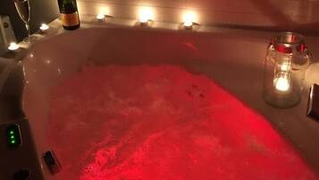 A hot tub with red lighting, a bottle, and candles.