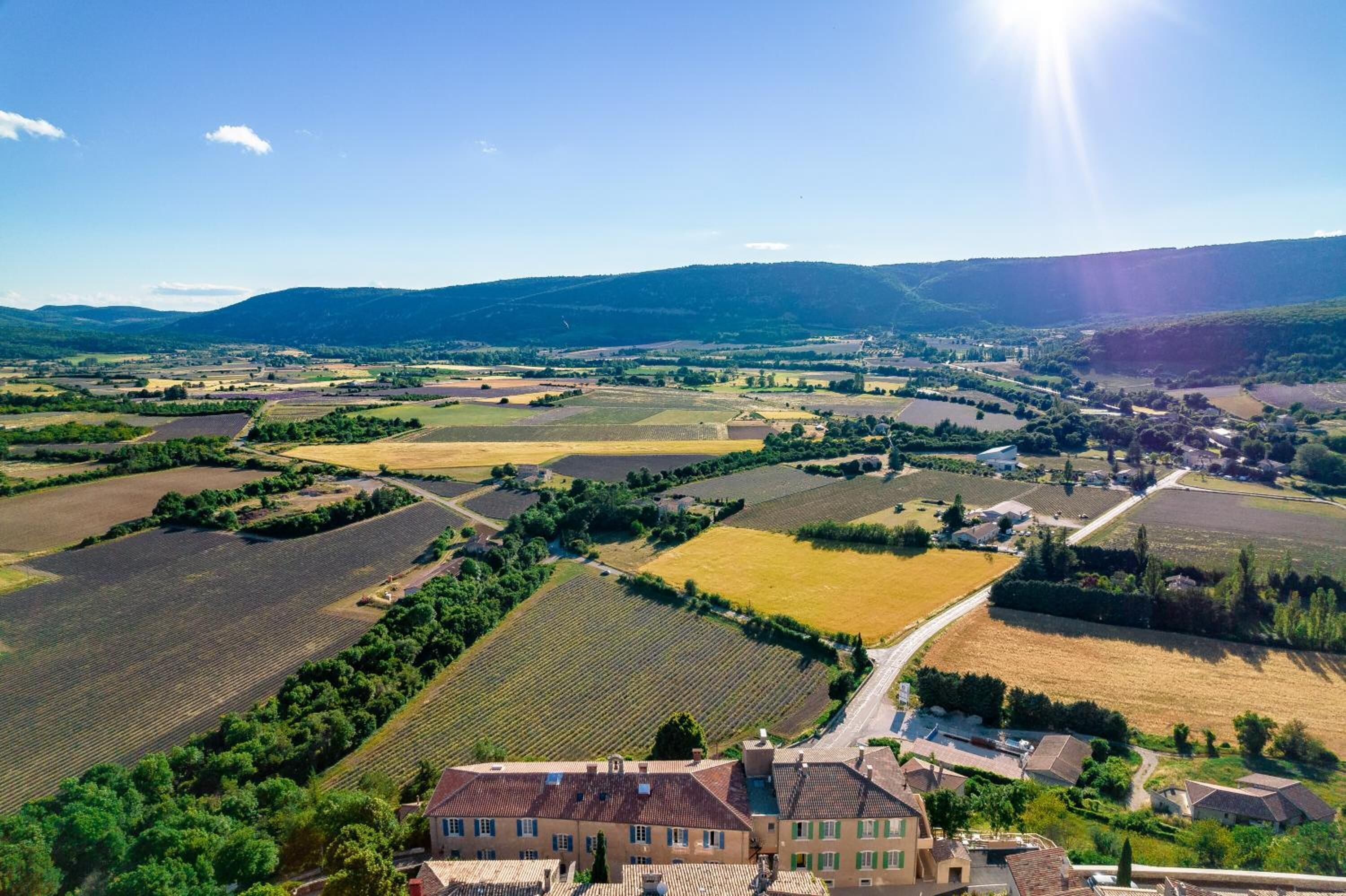 Une vue aérienne d’un paysage rural, avec des champs, une route sinueuse et un ensemble de bâtiments à l’architecture traditionnelle.