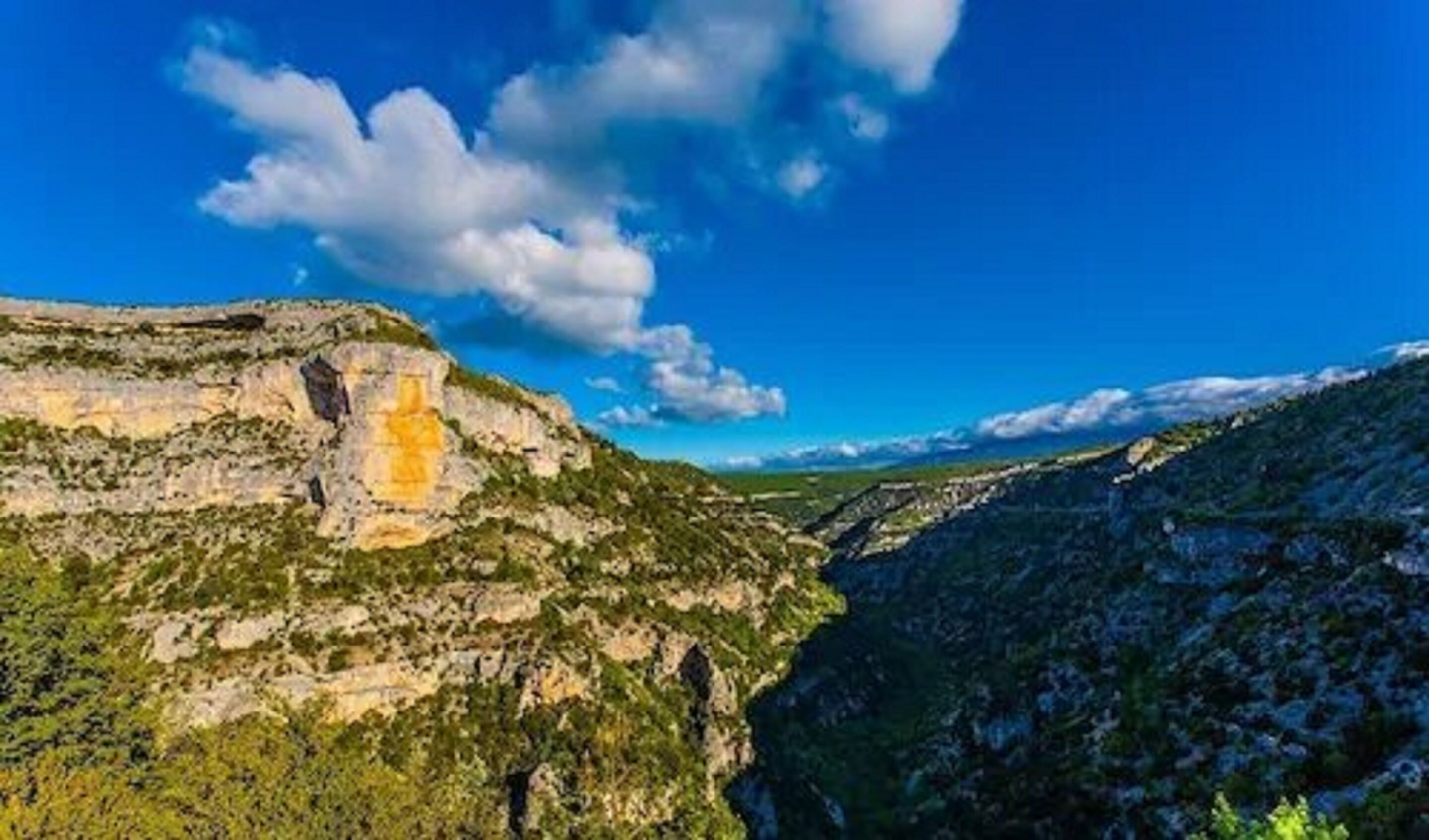 A mountainous landscape with a prominent cliff face and a valley.