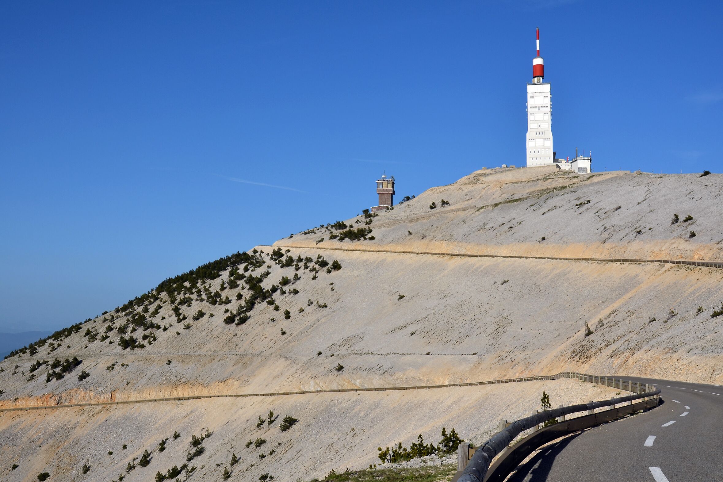 A winding road on a hillside with a lighthouse and a small tower in the distance.