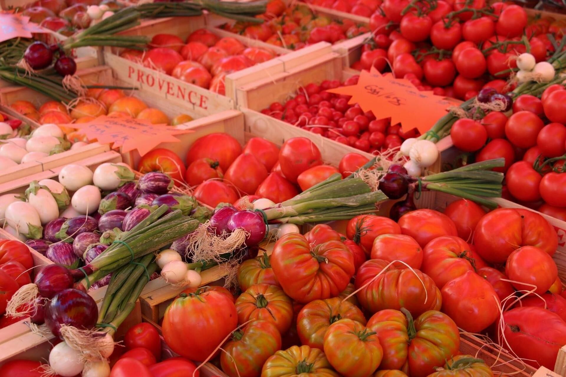 Puesto de mercado con varios vegetales, entre ellos tomates, cebollas y berenjenas.