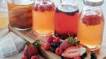 Four glass bottles with different colored liquids, possibly fruit juices, and fresh berries like strawberries and raspberries on a wooden surface.