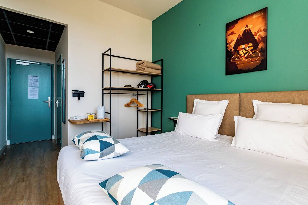 Une chambre d’hôtel avec un lit, un mur vert, un tableau encadré et une tête de lit en bois.
