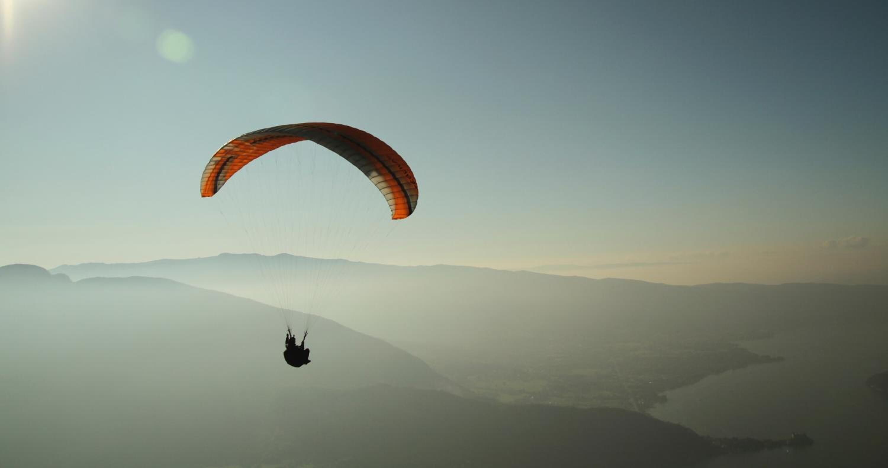 A paraglider in flight over a mountainous landscape.