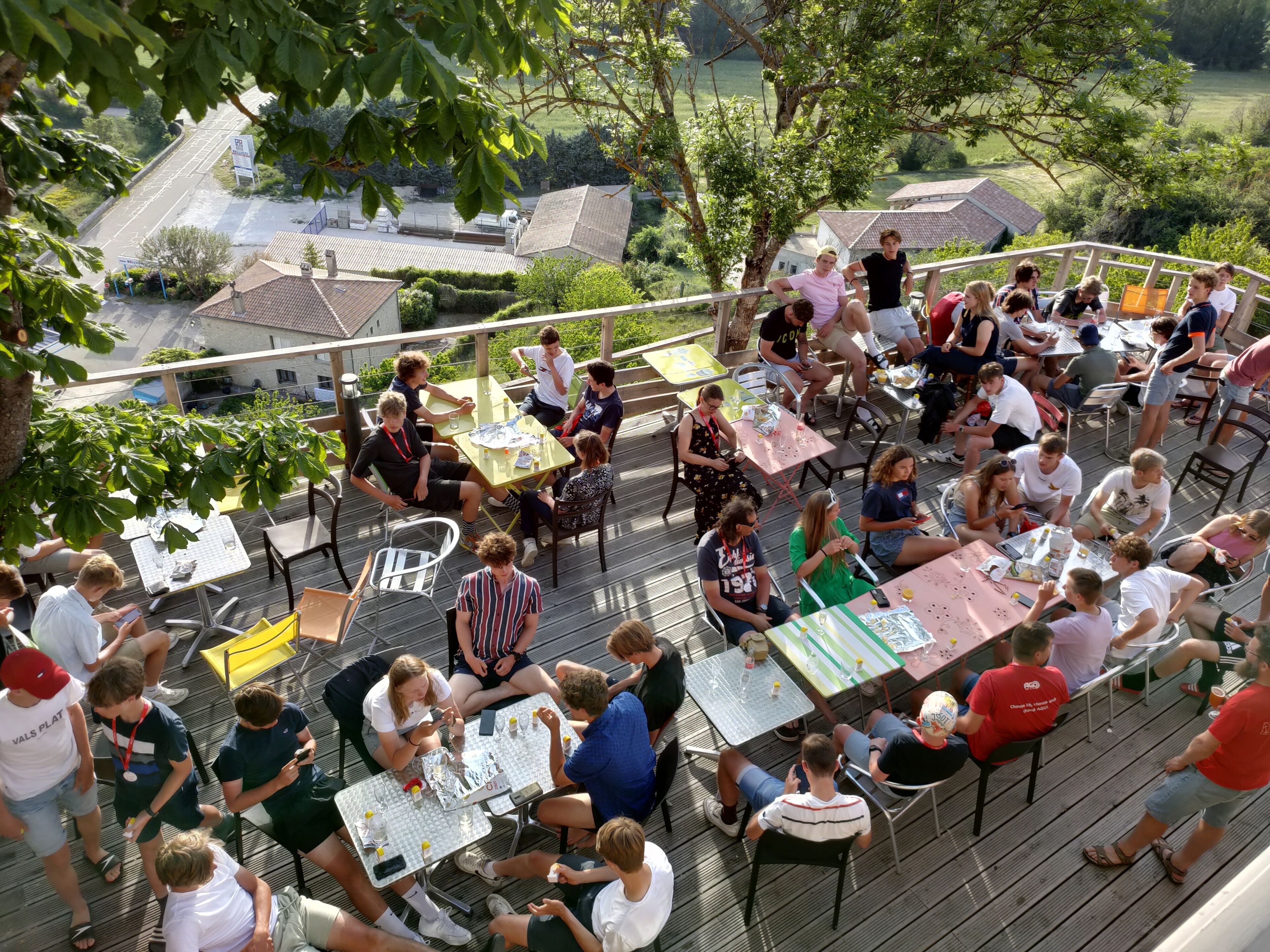 Um grupo de pessoas sentadas a mesas em um deck externo, com vista para uma área residencial.