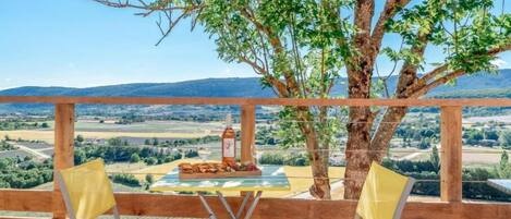 Una terraza de madera con dos sillas amarillas y una mesa dispuesta para una comida, con vistas a un paisaje pintoresco.