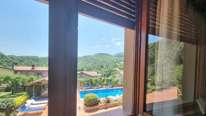 A view through a window of a pool area with a clear sky, surrounded by greenery and hills. - Villa Piazza, private solar heated pool,  walk to all facilities!  WIFI (Piazza al Serchio)