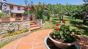 A garden with a stone wall, a potted plant with red flowers, and a building with a tiled roof and windows. - Villa Piazza, private solar heated pool,  walk to all facilities!  WIFI (Piazza al Serchio)