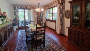 A dining area with a wooden table, chairs, a chandelier, and a large window with curtains. - Villa Piazza, private solar heated pool,  walk to all facilities!  WIFI (Piazza al Serchio)