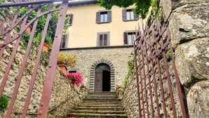 A stone staircase leading to a building with a dark wooden door, surrounded by a metal fence and potted plants. - Palazzo  Pasquini, stunning views/sunsets, private pool, WIFI, chef option!  (Treppignana Fosciandora)
