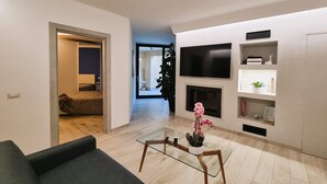 A modern living room with a sofa, glass coffee table, and a fireplace. There is a TV mounted on the wall and a plant on the floor. - Luxury villa, mountain views, private pool, WiFi & chef night option! (Nicciano)