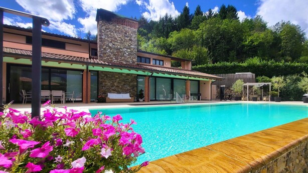 A modern house with a swimming pool, stone facade, and lush greenery in the background. - Luxury villa, mountain views, private pool, WiFi & chef night option! (Nicciano)
