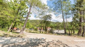 A gravel path leading through a wooded area with trees and a house in the background. - The Maison Rose studio (Callas)