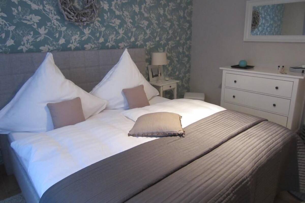 A neatly made bed with a striped bedspread and two pillows, a bedside table with a lamp, and a dresser with drawers.