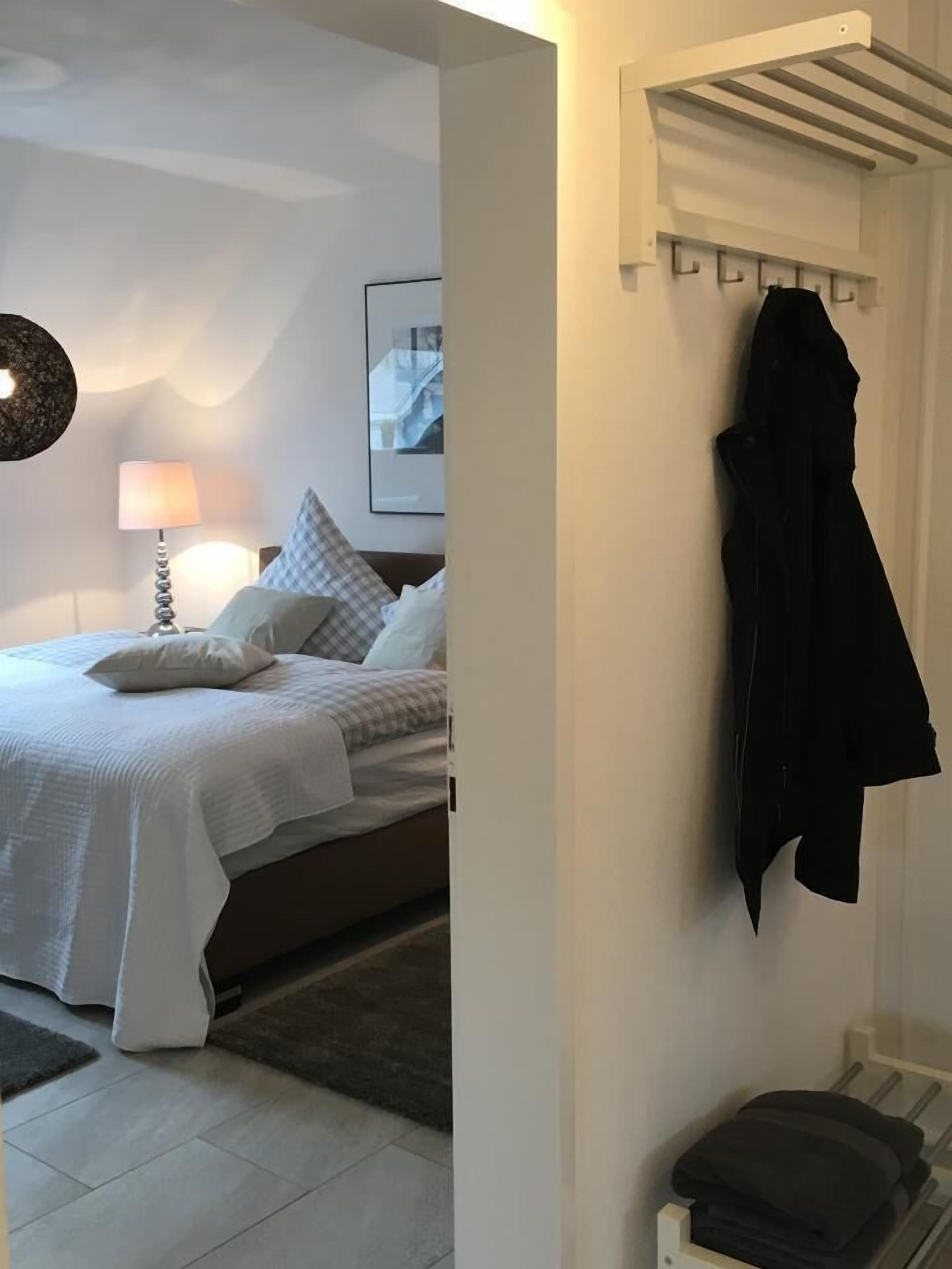 Ein Hotelzimmer mit einem Bett, einer Lampe, einem Kleiderhaken und einem gerahmten Bild an der Wand.