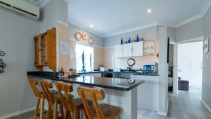 Een moderne keuken met een centraal eiland, houten barkrukken en een klok aan de muur.