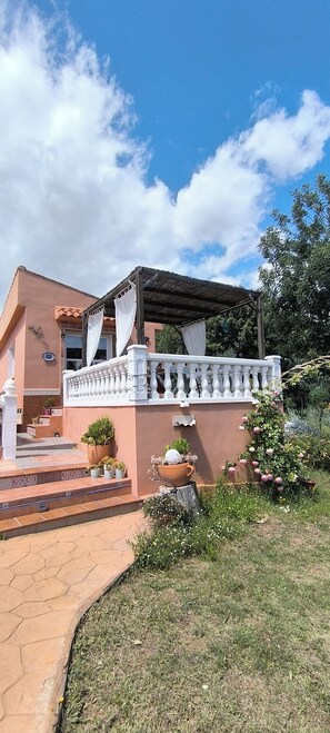 A building with a covered patio, a white balustrade, and a garden with potted plants.