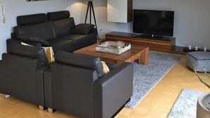 Ein modernes Wohnzimmer mit einer schwarzen Ledersofa, einem Holztisch, einem Flachbildfernseher und einer Stehlampe.