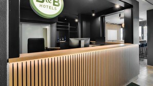 A reception desk with a B&B Hotels logo, a wooden reception area, and a modern interior design. - B&B Hotel München-Garching (Garching)