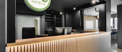 Un mostrador de recepción con el logotipo de B&B Hotels, zona de recepción de madera y diseño de interiores moderno.