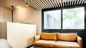 A modern living room with a leather sofa, a white cabinet, and a large window with a view of trees. - B&B Hotel München-Garching (Garching)