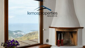 A room with a large window overlooking a coastal landscape, a fireplace, and a hanging light fixture. - Pool garden house (Kea)