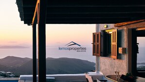 A terrace with a view of the sea, a table with a glass of wine, and a sign for lemosproperties real estate. - Pool garden house (Kea)