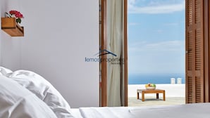 A bedroom with a bed, a wooden shelf with flowers, a view of the beach, and a table with fruit. - Pool garden house (Kea)